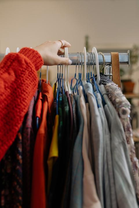 A shopper reaches for clothes on a thrift store rack. 