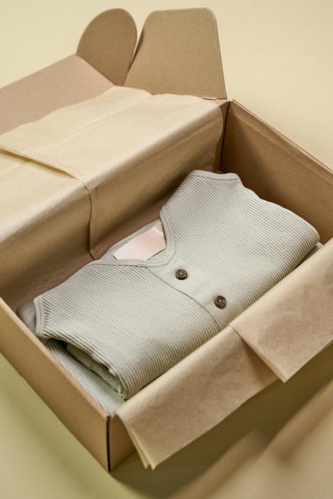 A green sweater in a box with a blank care label. 