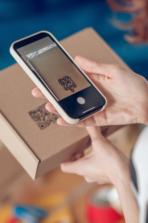 woman scanning QR code on box with phone - QR codes and other 2D barcodes can help brands communicate ESG and sustainability information