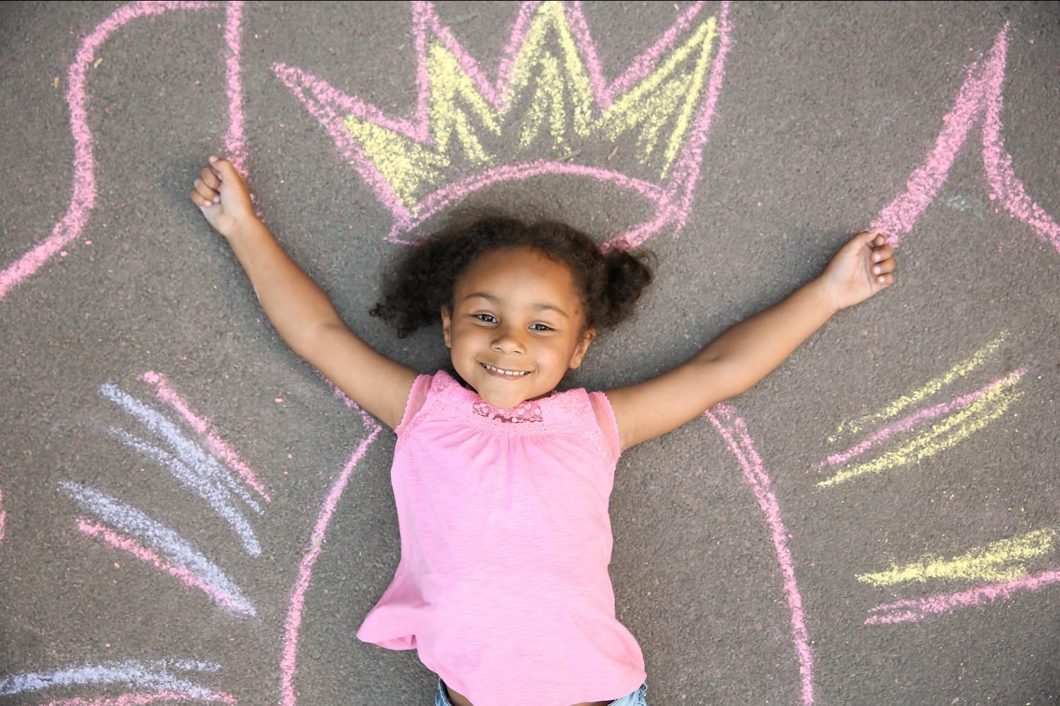 little girl laying on a chalk outline of a queen crown - chase your dreams