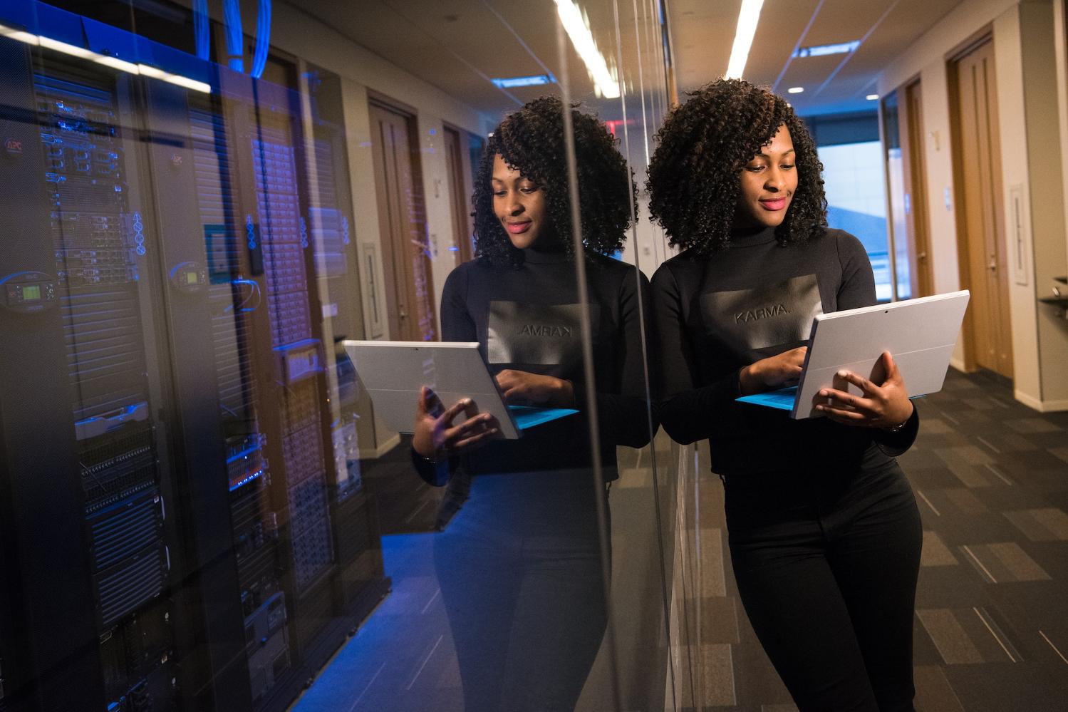 A photo of a woman and her reflection working on a laptop in front of a server room - soft skills for tech leaders
